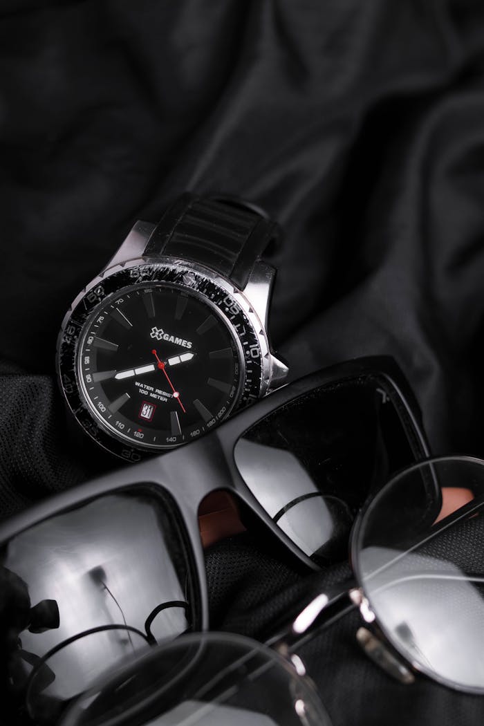 Close-up of a watch and eyewear on dark fabric, highlighting luxury fashion accessories.